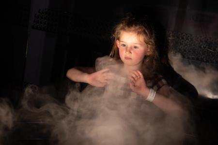 Girl playing with the smoke machine in the dark room at Techniquest